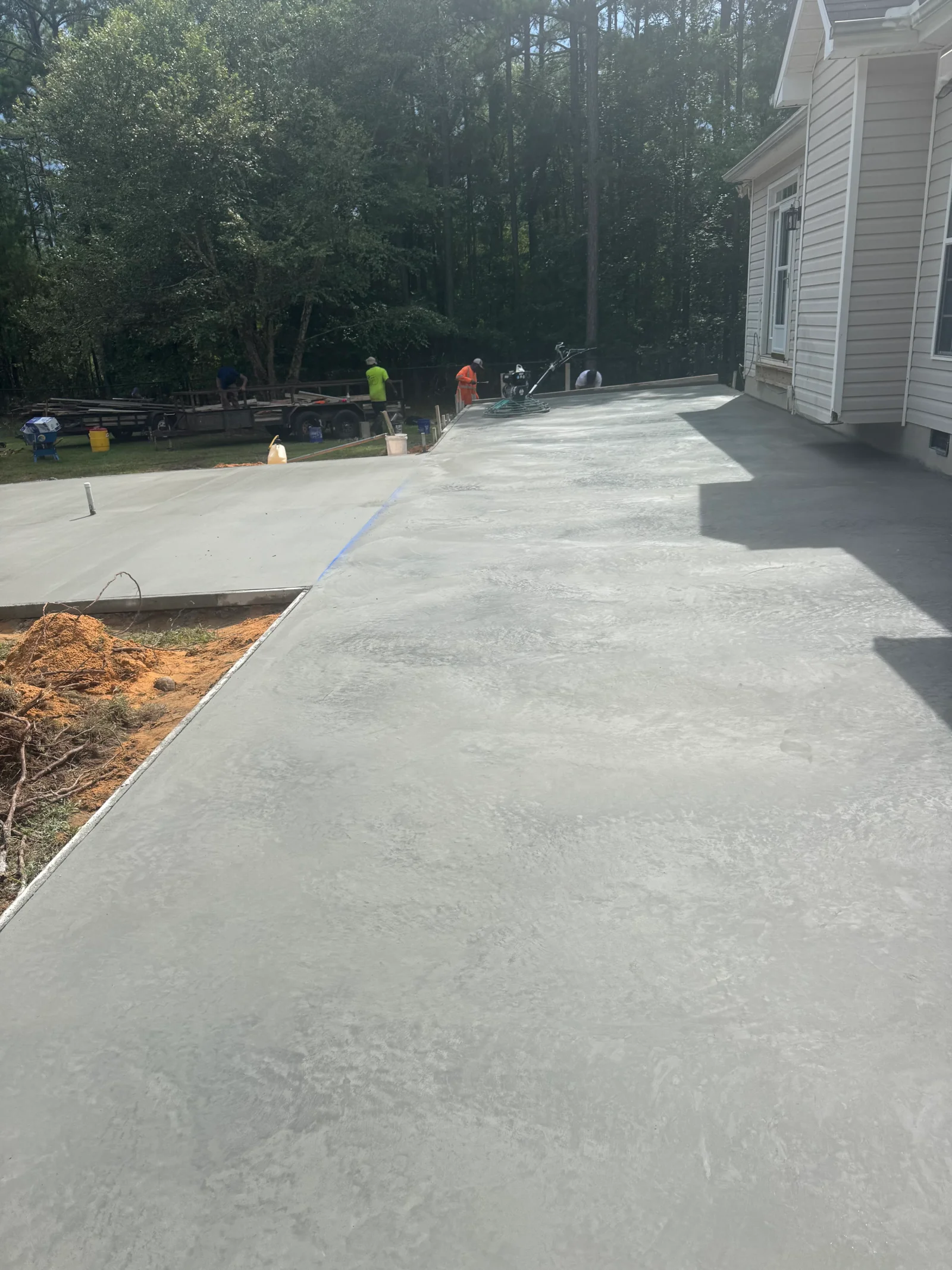 Fresh concrete driveway installation with finished surface and edge forms, crew working on-site