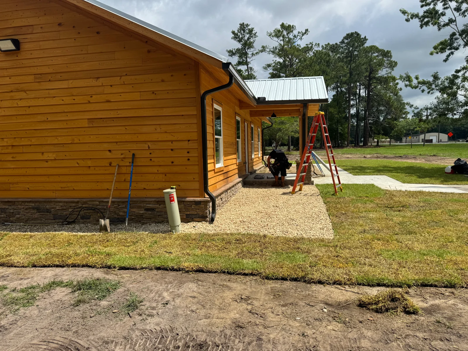 Concrete pad and gravel base installation next to log cabin with metal roof