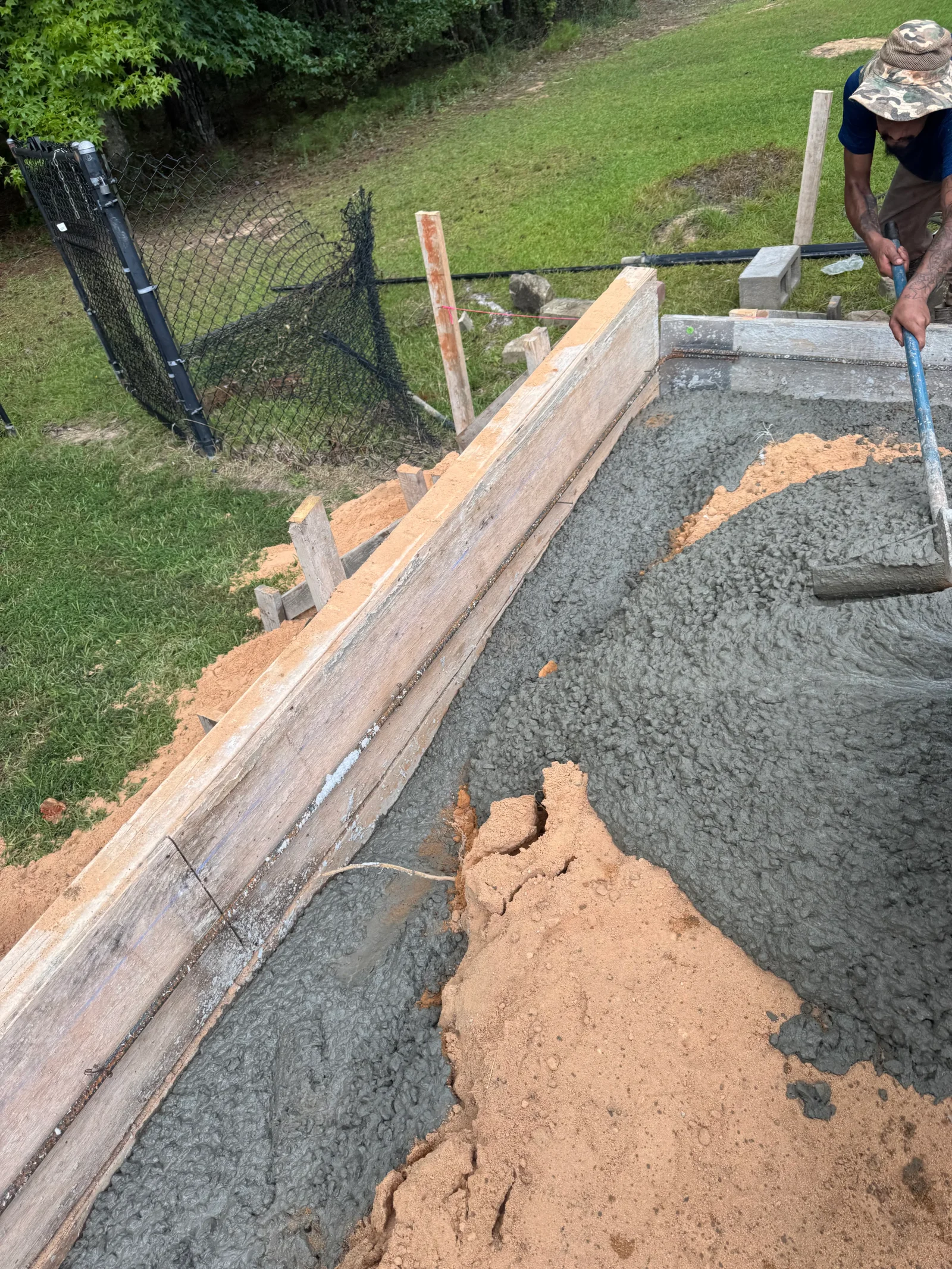 Concrete foundation excavation with wooden forms, clay fill, and landscape fabric installation